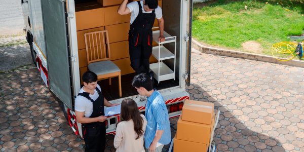 Asian Couple check while unloading boxes and furniture from a pickup truck to a new house with service cargo two men movers worker in uniform lifting boxes. concept of Home moving and delivery.